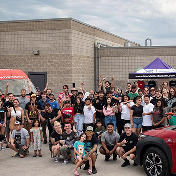 A large group of Summer Heat Subie Meet attendees are gathered outside at the event.