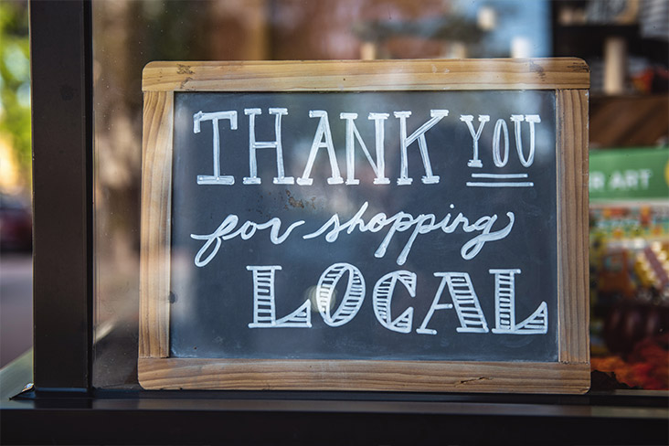 A black chalk board framed in wood that says, Thank you for shopping local in white chalk.