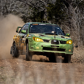A green vehicle is racing over a gravel road with a plume of brown dust trailing behind it. 
