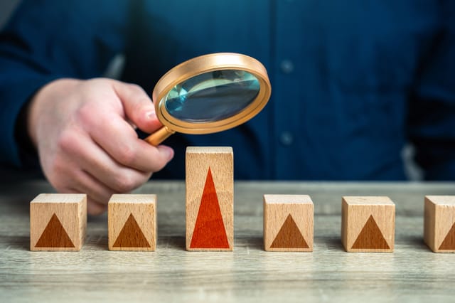 A hand holding a magnifying glass above several blocks containing pictures of triangles. The block directly under the magnifying glass is taller and has a larger triangle on it A hand holding a magnifying glass above several blocks containing pictures of triangles. The block directly under the magnifying glass is taller and has a larger triangle on it