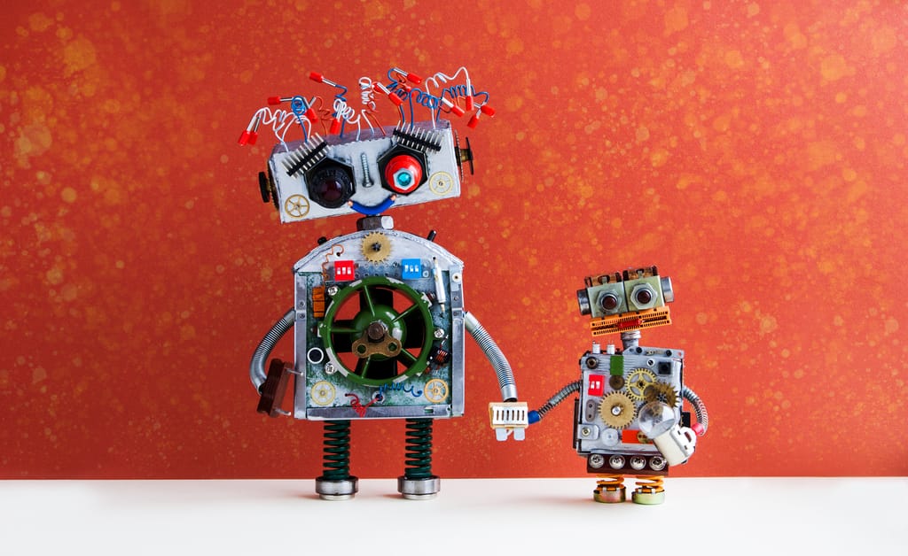 A large toy robot holding the hand of a smaller one, on a white floor against a red-orange background A large toy robot holding the hand of a smaller one, on a white floor against a red-orange background