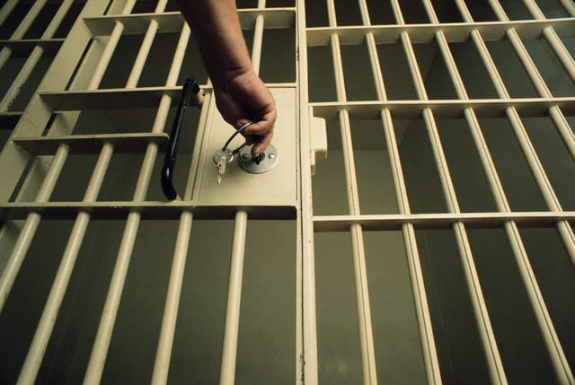 A photograph of a hand reaching out to lock a prison cell with a bunch of keys A photograph of a hand reaching out to lock a prison cell with a bunch of keys