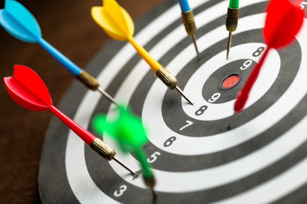 A close-up of seven darts on a dartboard, grouped around the center but all missing the bullseye. A close-up of seven darts on a dartboard, grouped around the center but all missing the bullseye.