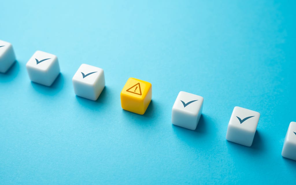 A row of white cubes on a blue background. The cubes contain checkmarks, with a yellow cube in the middle containing an alert symbol. A row of white cubes on a blue background. The cubes contain checkmarks, with a yellow cube in the middle containing an alert symbol.