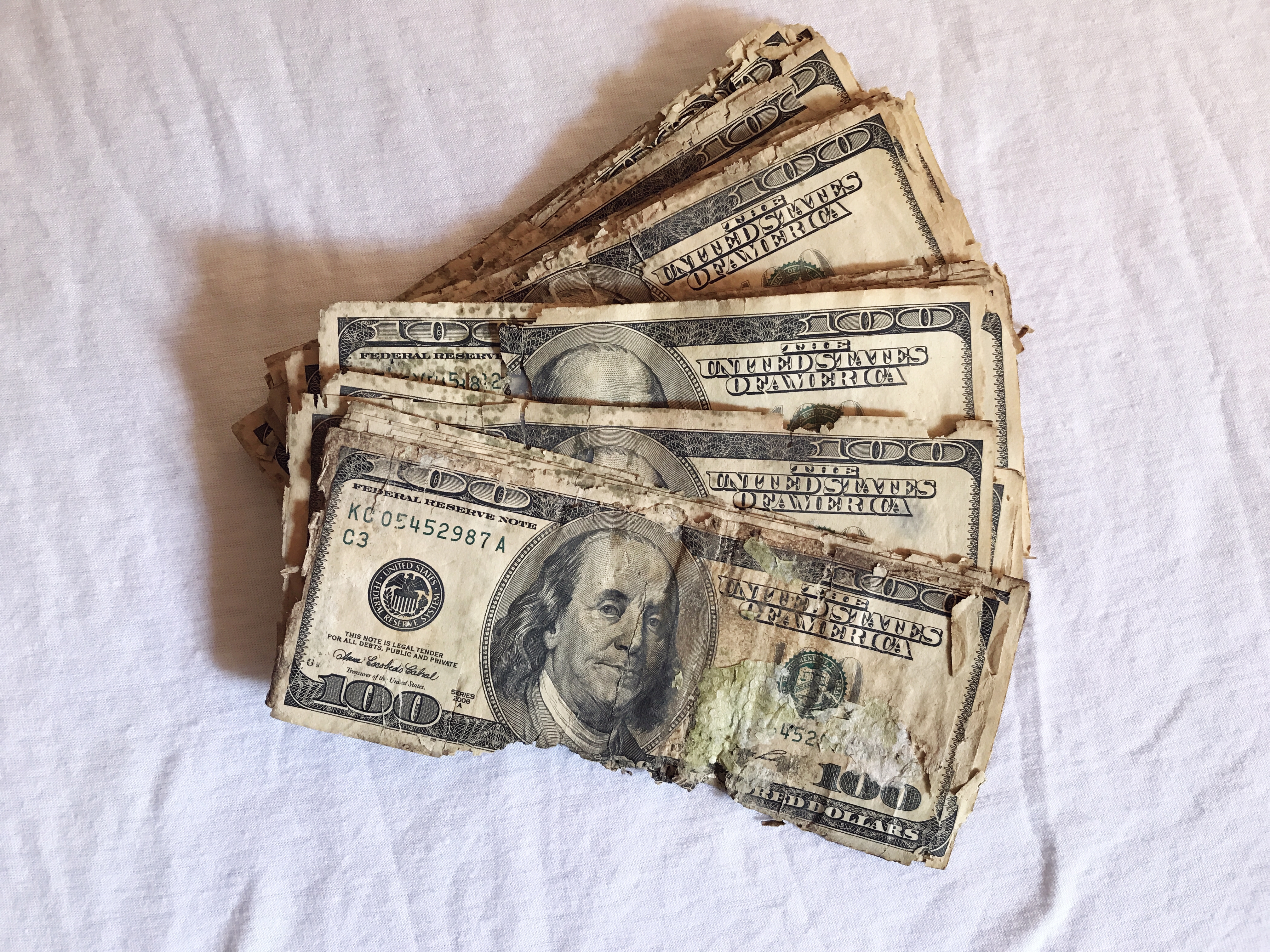 Several crumpled and dirty dollar bills fanned out on a white sheet