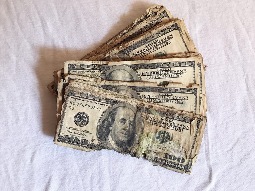 Several crumpled and dirty dollar bills fanned out on a white sheet