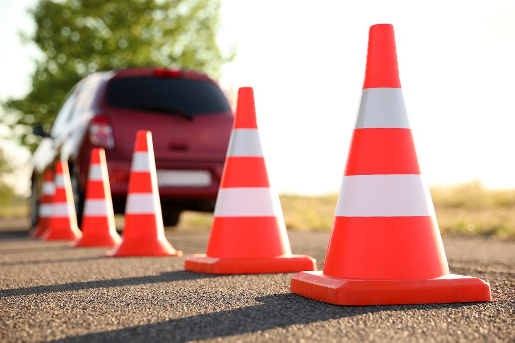 A line of traffic cones with a vehicle driving in the background away from the camera A line of traffic cones with a vehicle driving in the background away from the camera