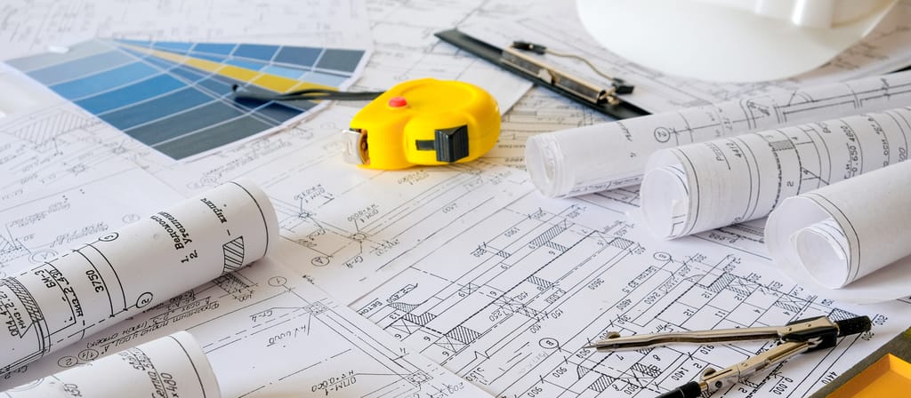 A photograph of architectural diagrams on a table, with a yellow tape measure A photograph of architectural diagrams on a table, with a yellow tape measure