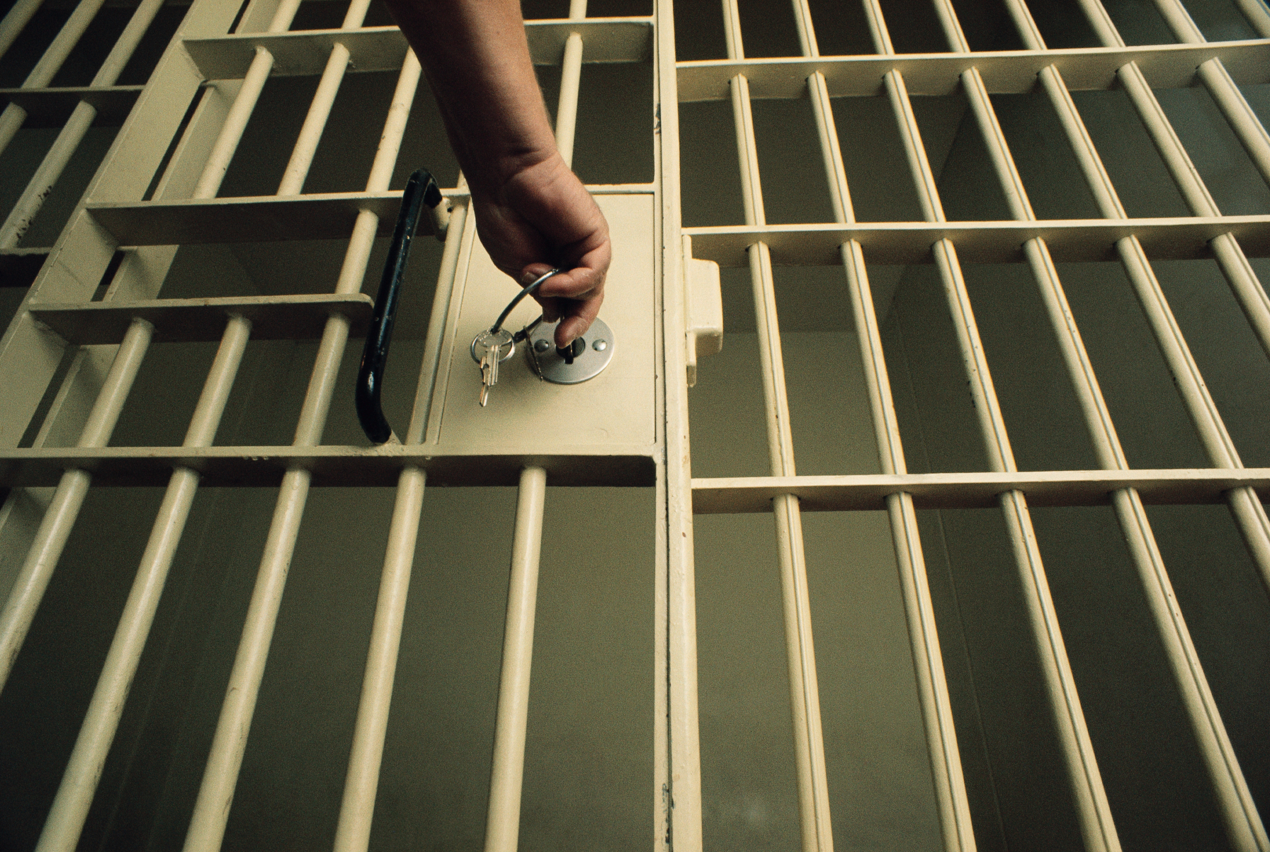 A photograph of a hand reaching out to lock a prison cell with a bunch of keys