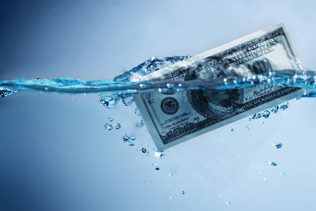 A photograph of a dollar-bill partly immersed in clear water, with bubbles
