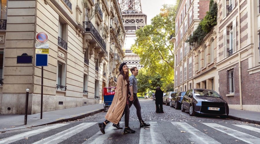 dos personas caminando en una calle de París con la torre Eiffel de fondo. 
