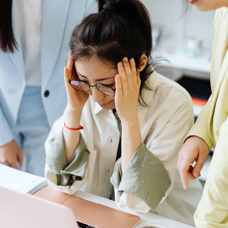 Mujer con dolor de cabeza en el trabajo por sentir presión social por no hablar inglés.