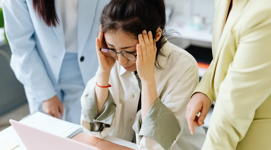Mujer con dolor de cabeza en el trabajo por sentir presión social por no hablar inglés.