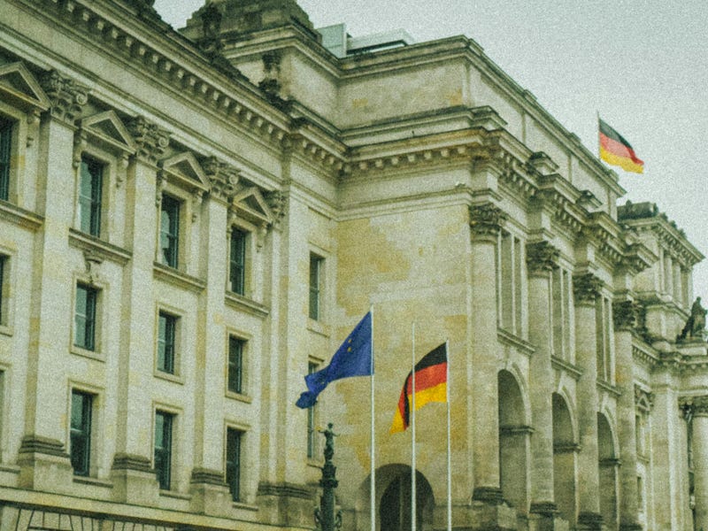 Varias personas caminan delante de un edificio con banderas alemanas.