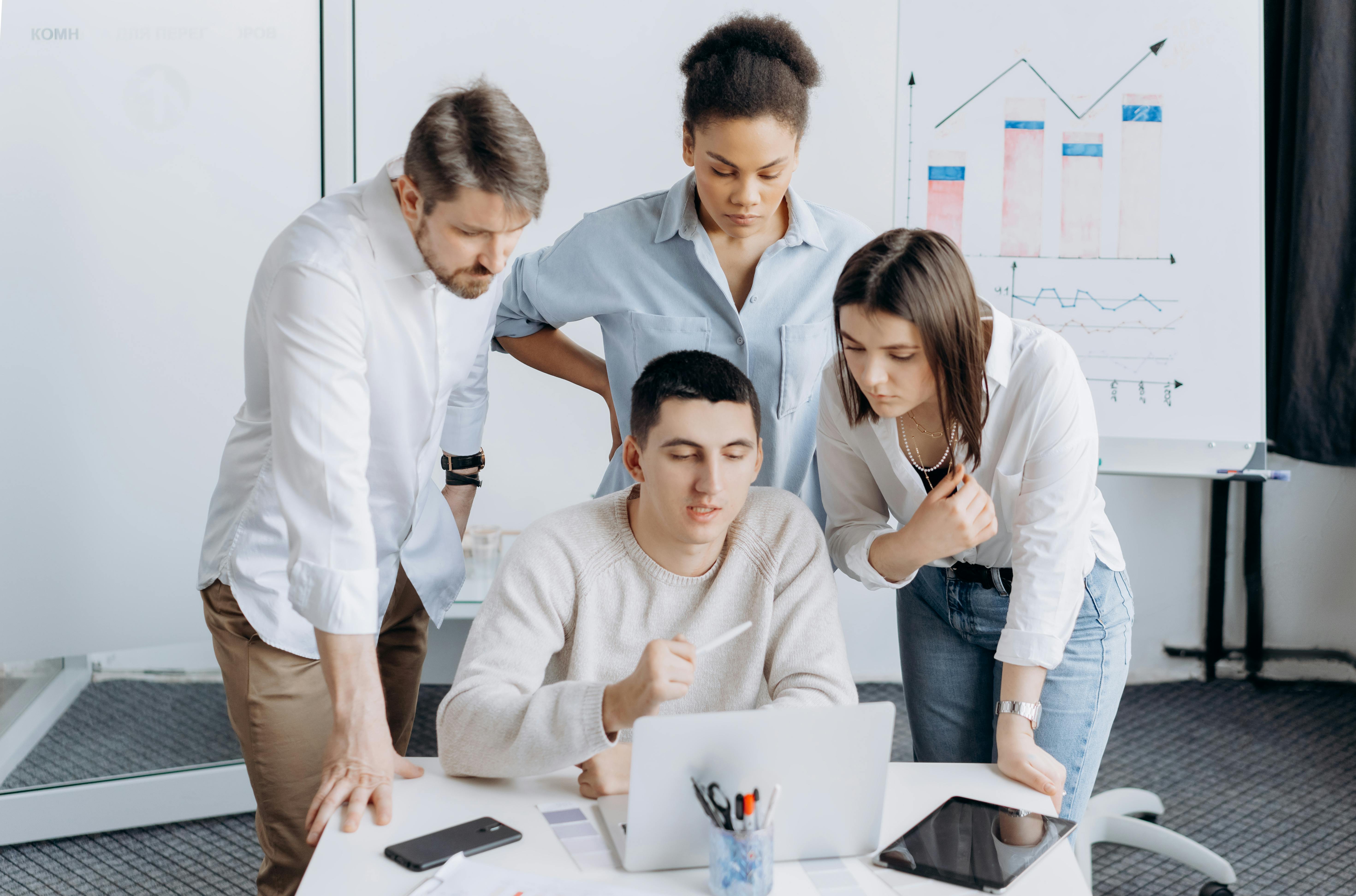 Equipo de trabajo multicultural colaborando frente a una computadora portátil en una reunión laboral, analizando información y gráficos en un entorno corporativo.