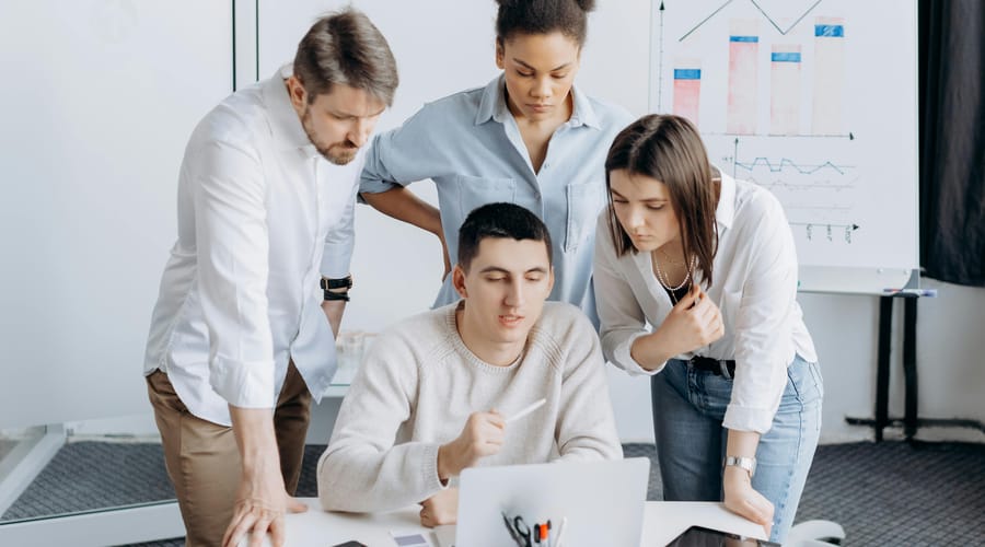 Equipo de trabajo multicultural colaborando frente a una computadora portátil en una reunión laboral, analizando información y gráficos en un entorno corporativo.