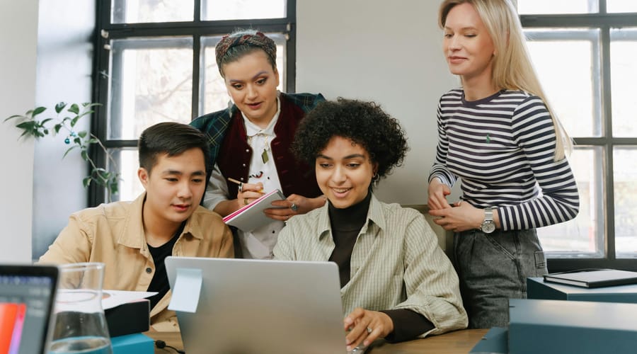 Grupo de adultos reunidos frente a una computadora portátil, estudiando sobre el proceso de aprendizaje.
