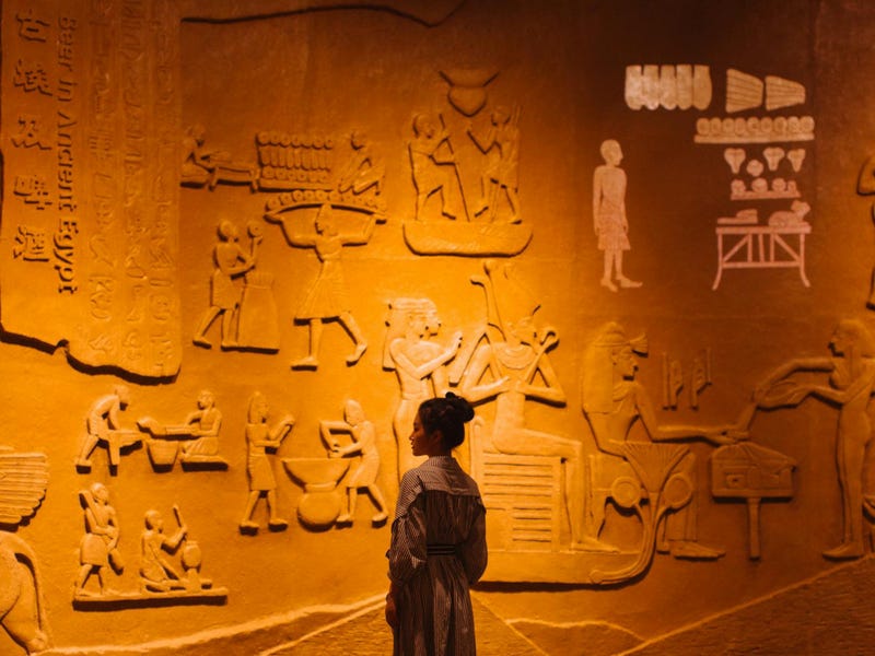 Una mujer visita un museo egipcio, uno de los idiomas antiguos, con escritos e imágenes en la pared.