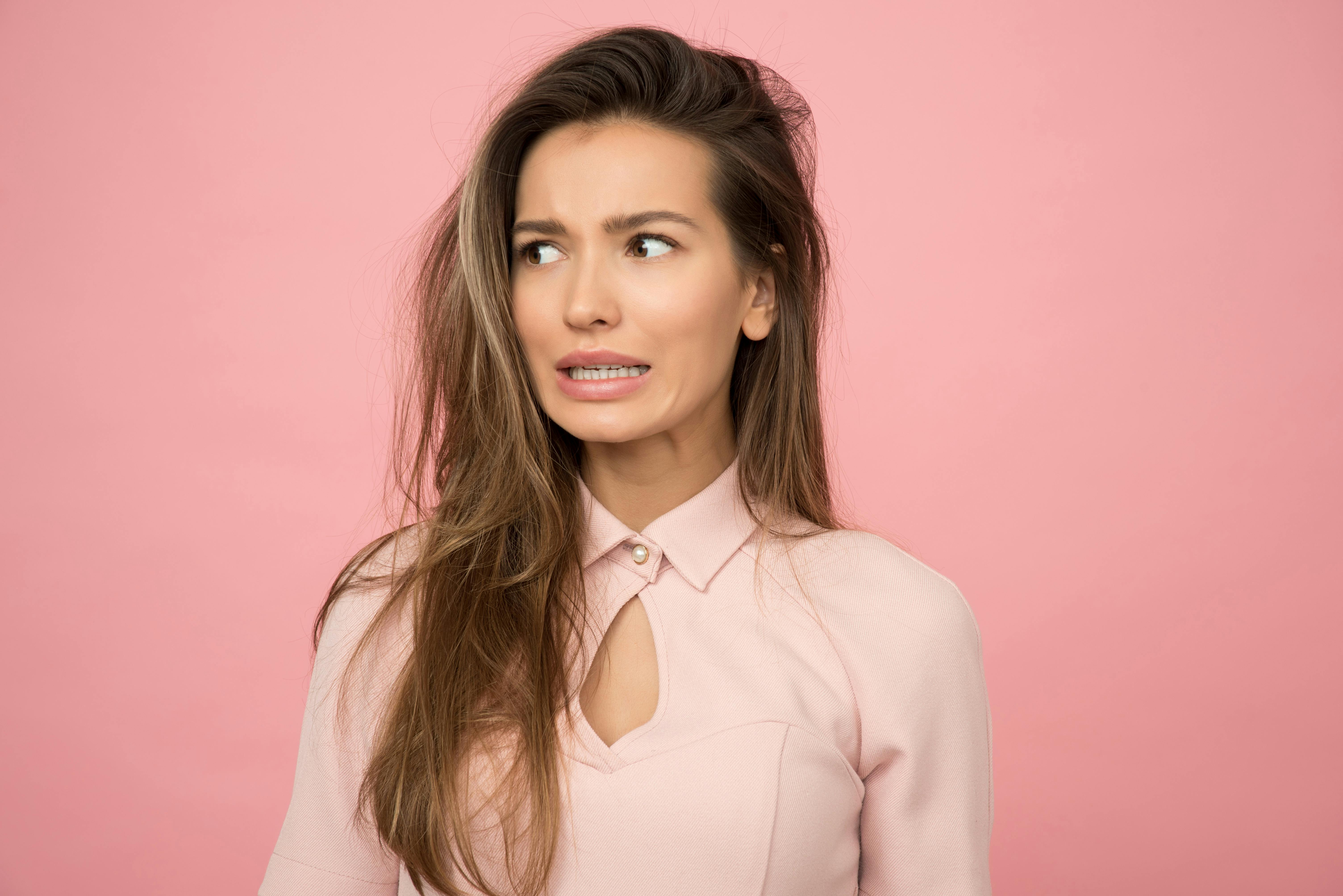 Mujer con cara de preocupación por olvidar su idioma natal. Fondo rosa.