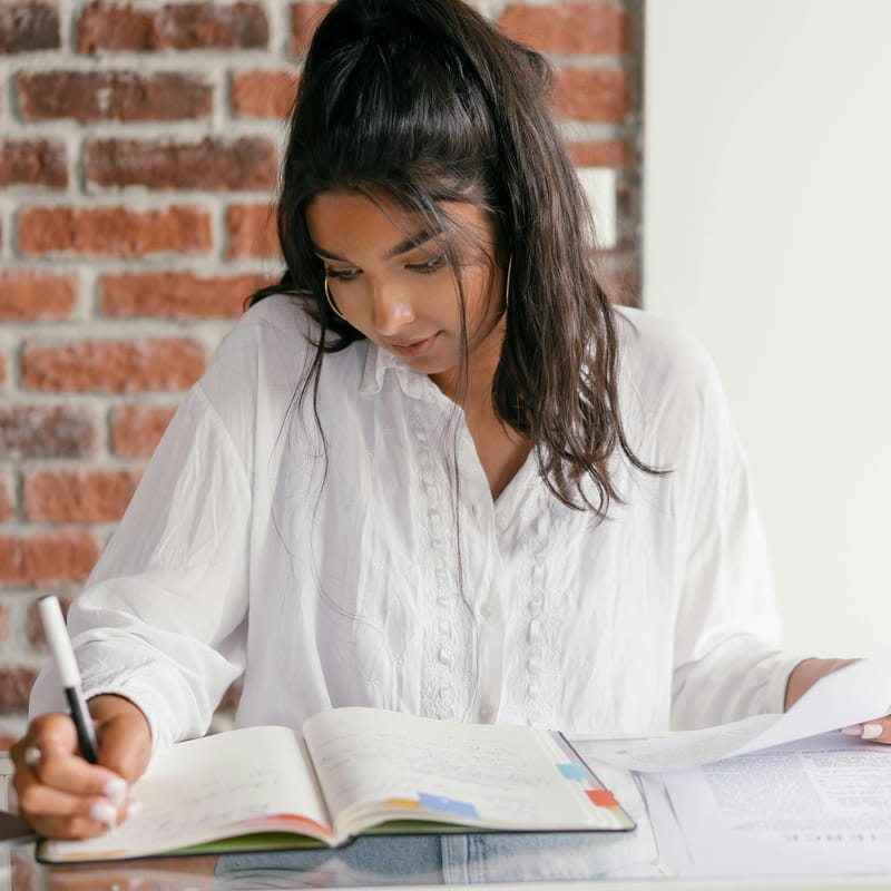 Mujer estudiando con su libro sobre verbos en portugués.