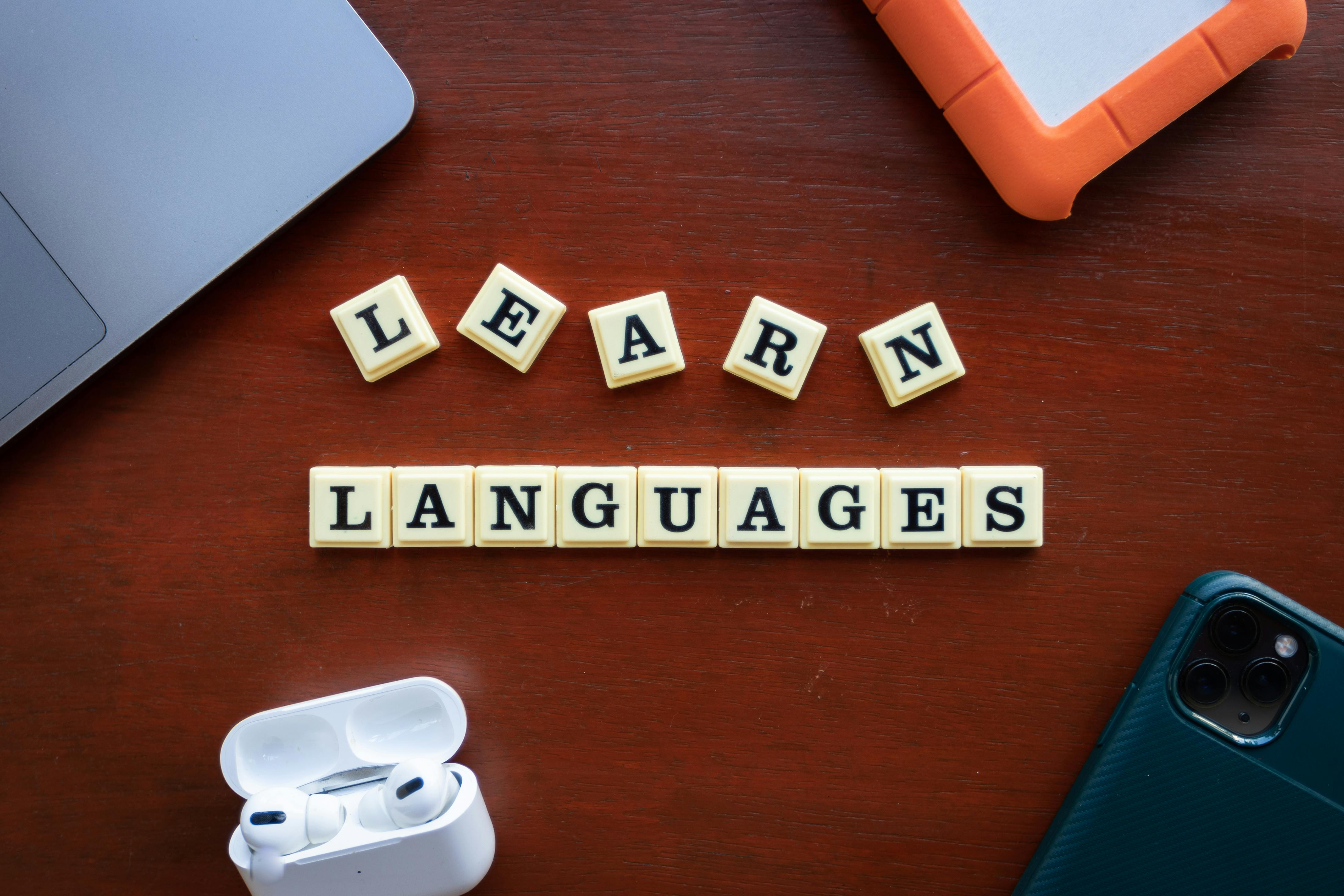Fichas con la frase “Learn Languages” sobre un escritorio, junto a audífonos, un celular y una laptop, simbolizando el aprendizaje de idiomas.