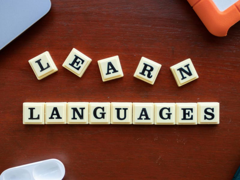 Fichas con la frase “Learn Languages” sobre un escritorio, junto a audífonos, un celular y una laptop, simbolizando el aprendizaje de idiomas.