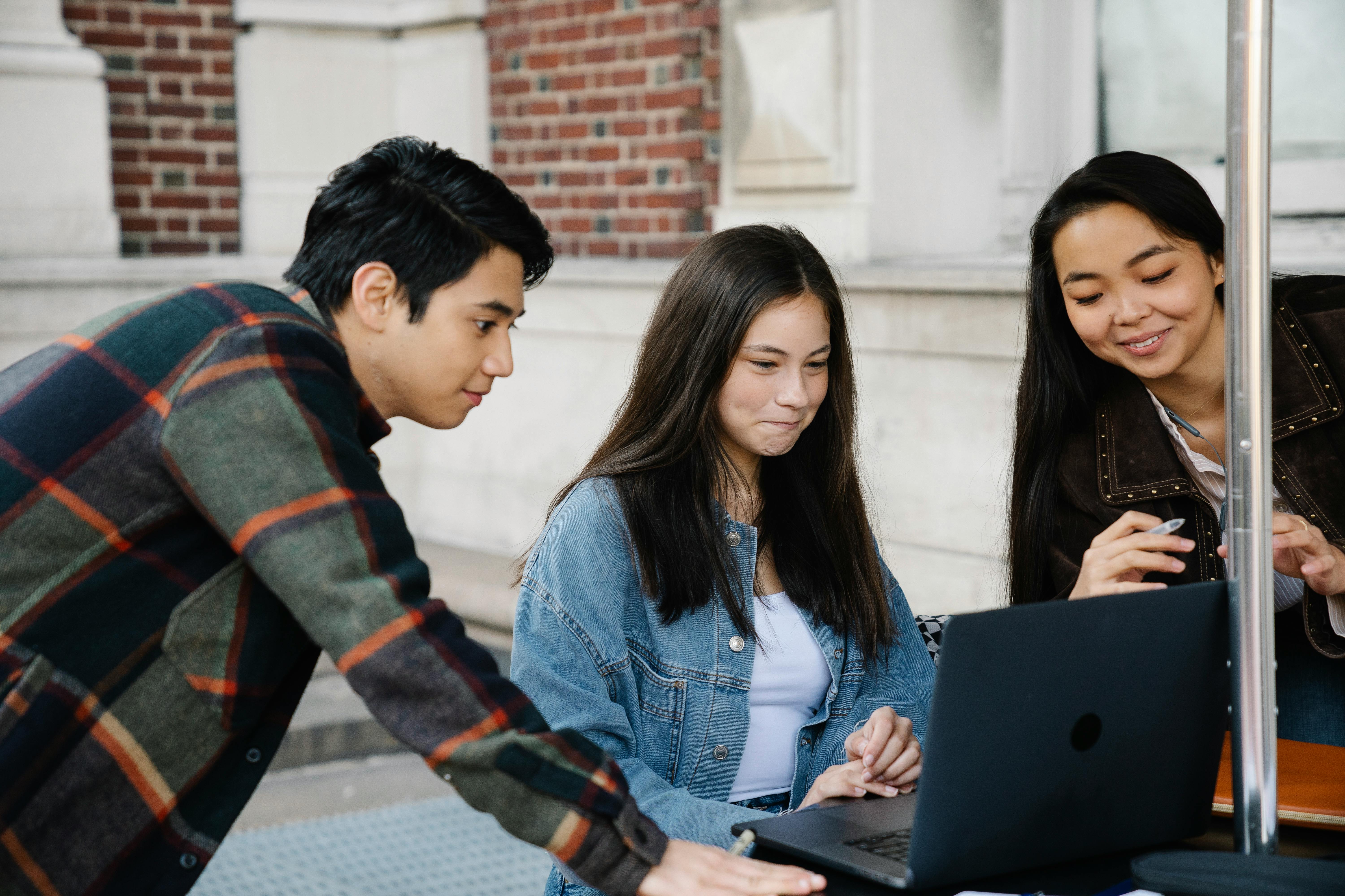 Tres estudiantes jóvenes colaboran frente a una laptop en un entorno universitario para estudiar temas de inglés c1.