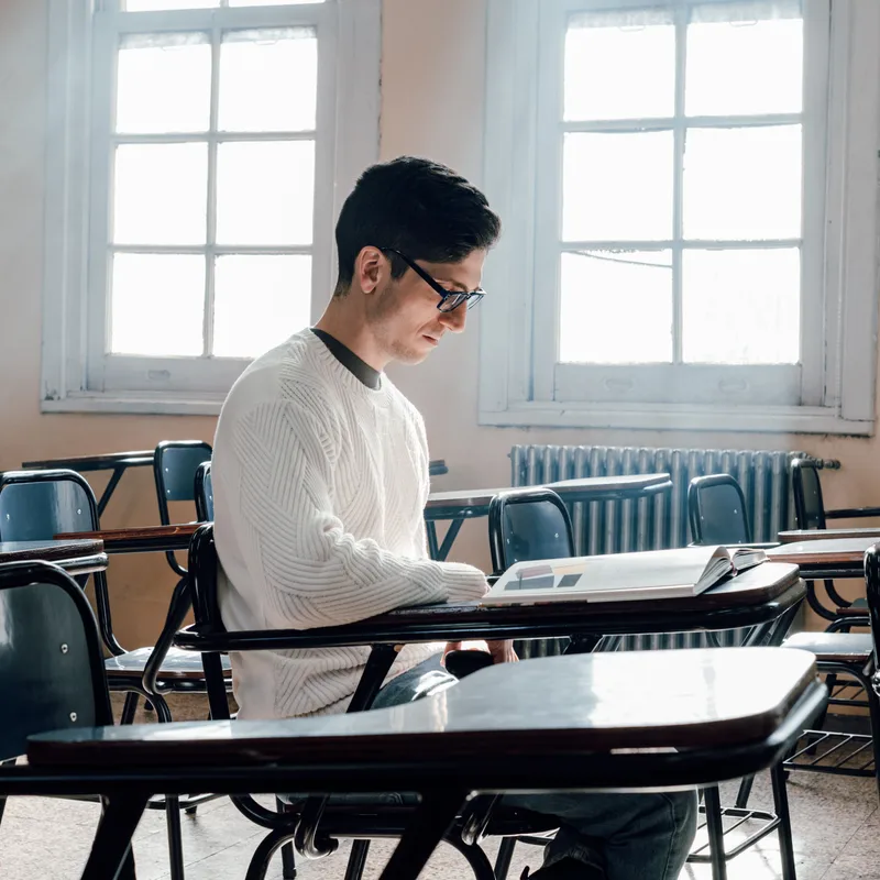 Estudiante en salón leyendo un libro sobre verbos copulativos en inglés.