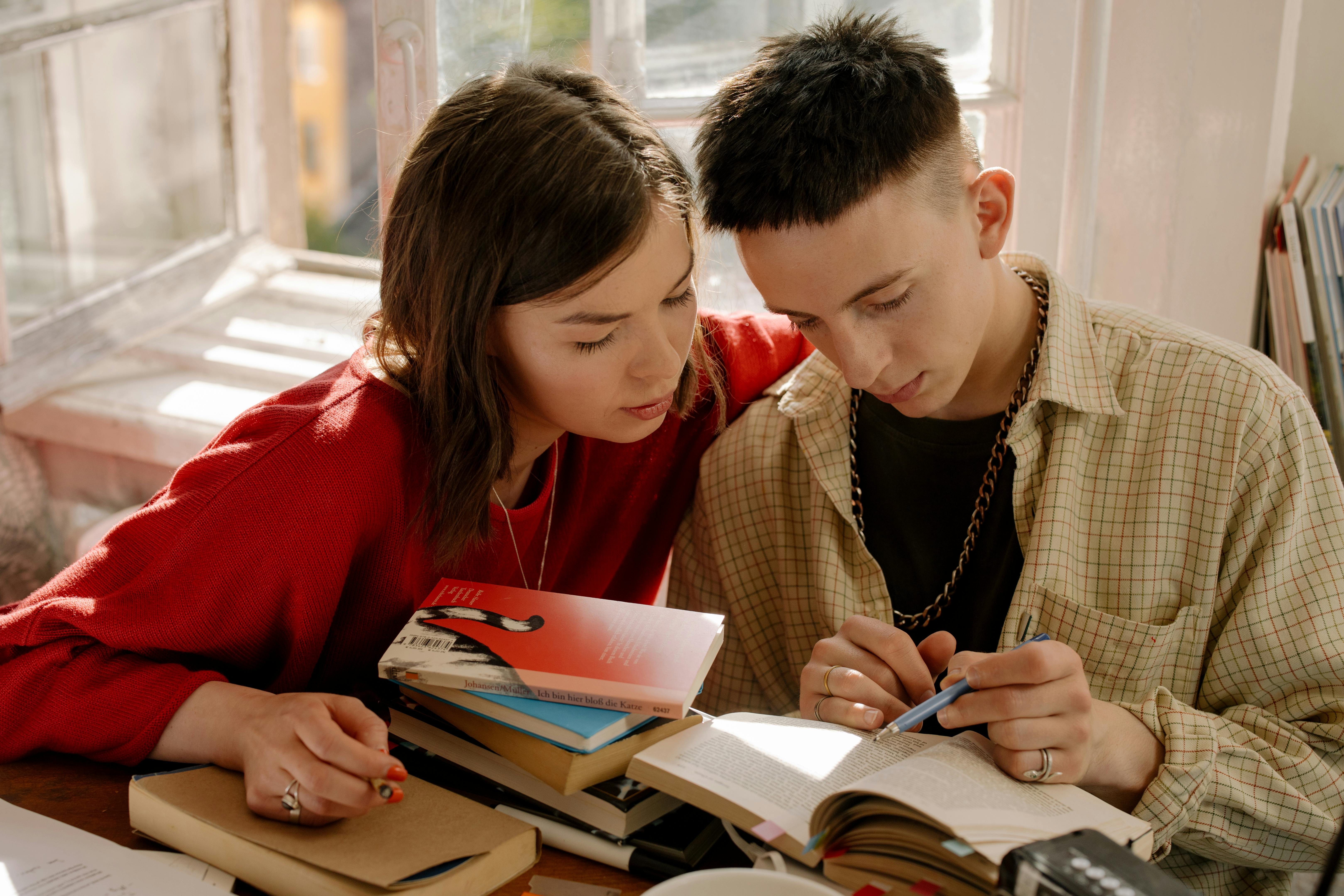 Dos jóvenes sentados leyendo un libro juntos, acompañados de varios libros sobre cuál es el idioma más antiguo del mundo.