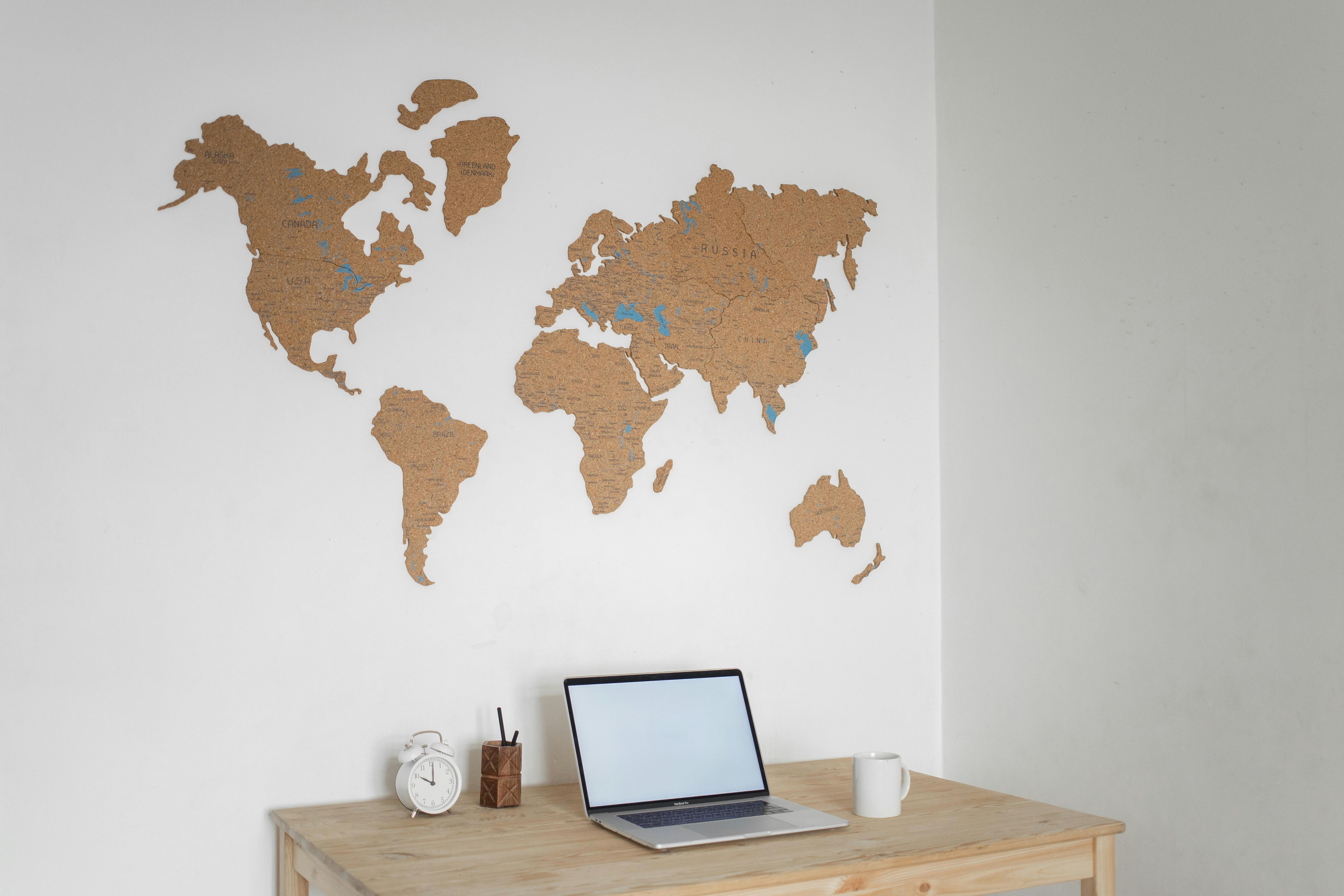Un escritorio con un mapa del mundo en la pared, un reloj, una taza y una laptop para representar el mercado laboral.