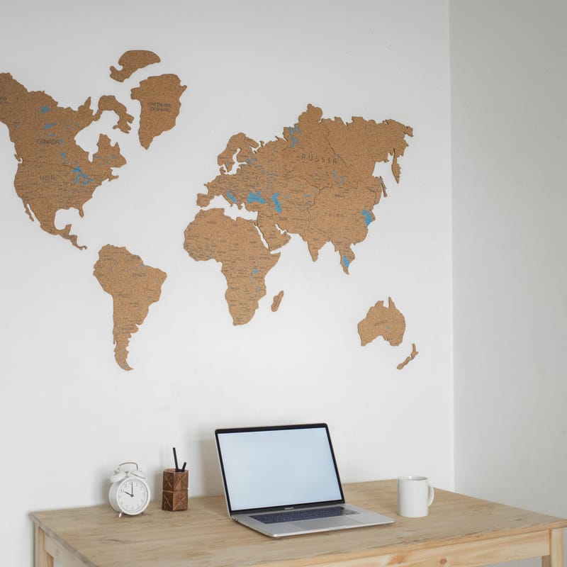 Un escritorio con un mapa del mundo en la pared, un reloj, una taza y una laptop para representar el mercado laboral.