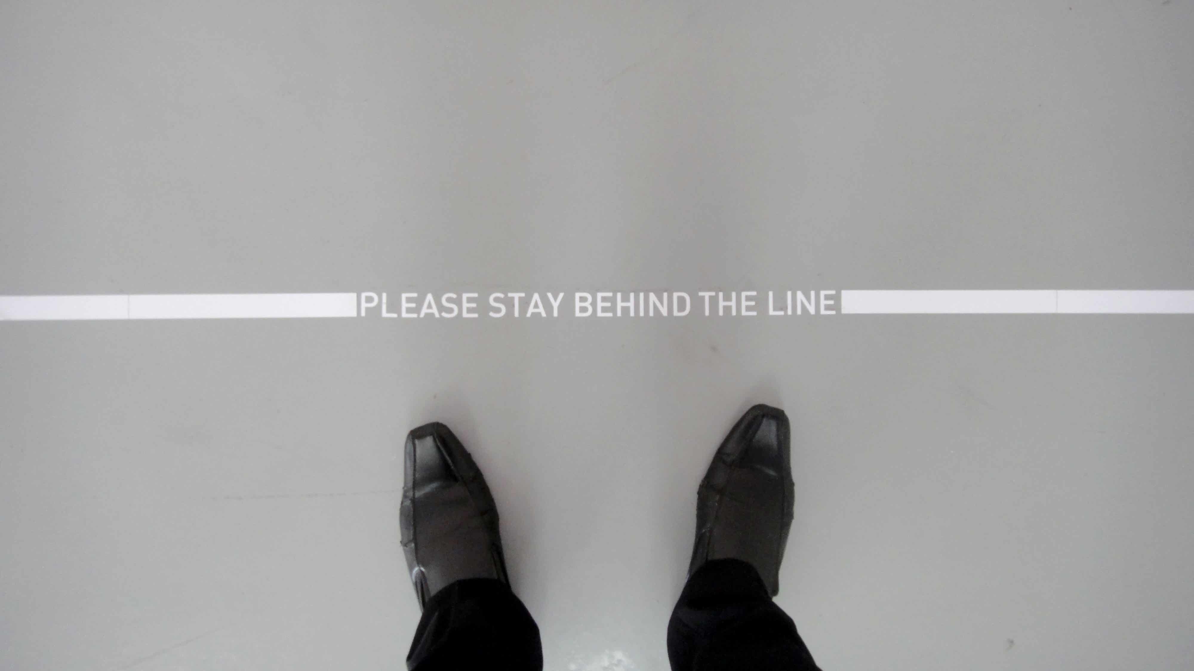 Someone standing behind a line that reads "Please stay behind the line".