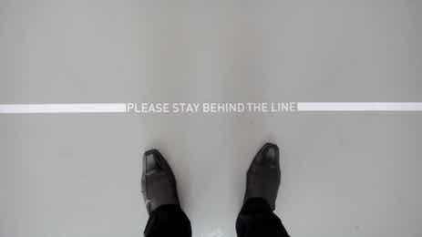 Someone standing behind a line that reads "Please stay behind the line".