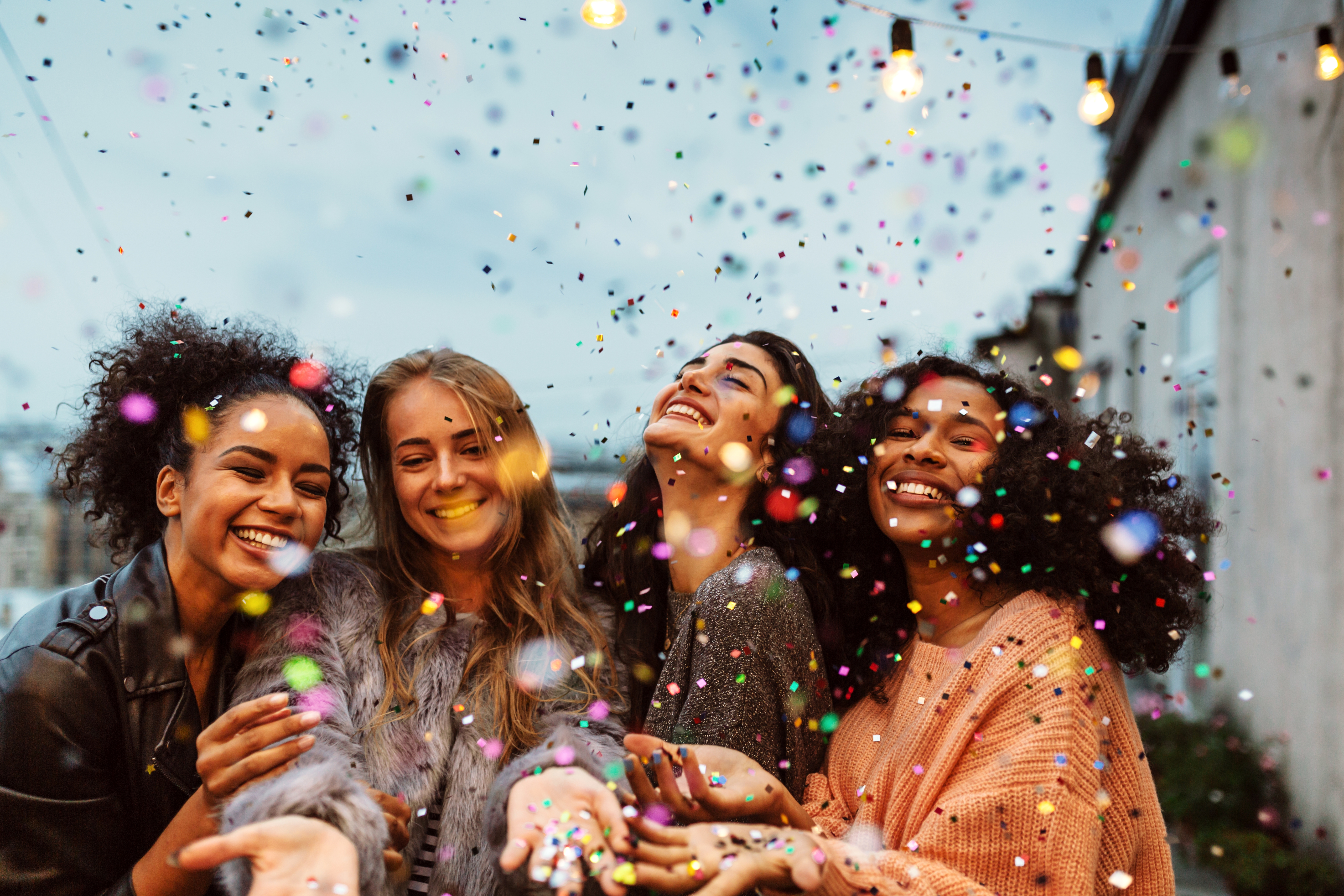 Cuatro amigas de distintas etnias se ríen y celebran bajo una lluvia de confeti.