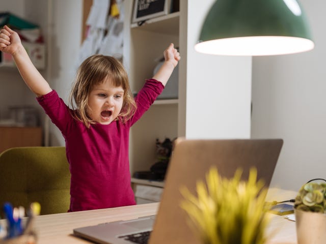 Una niña pequeña celebra con los brazos en alto frente a una laptop, emocionada por lo que ve.