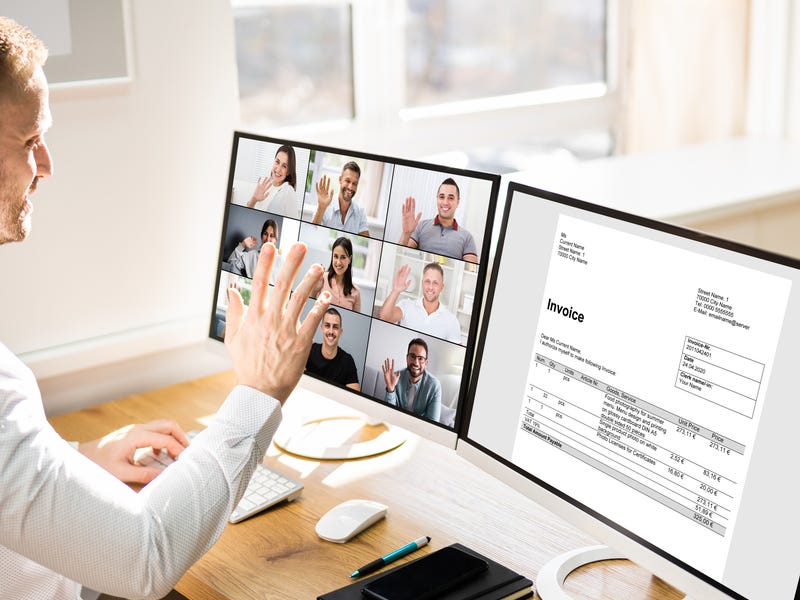 Hombre saluda en videollamada empresarial en dos monitores, comunicación virtual con Berlitz.