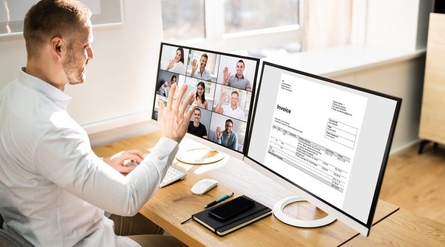 Hombre saluda en videollamada empresarial en dos monitores, comunicación virtual con Berlitz.