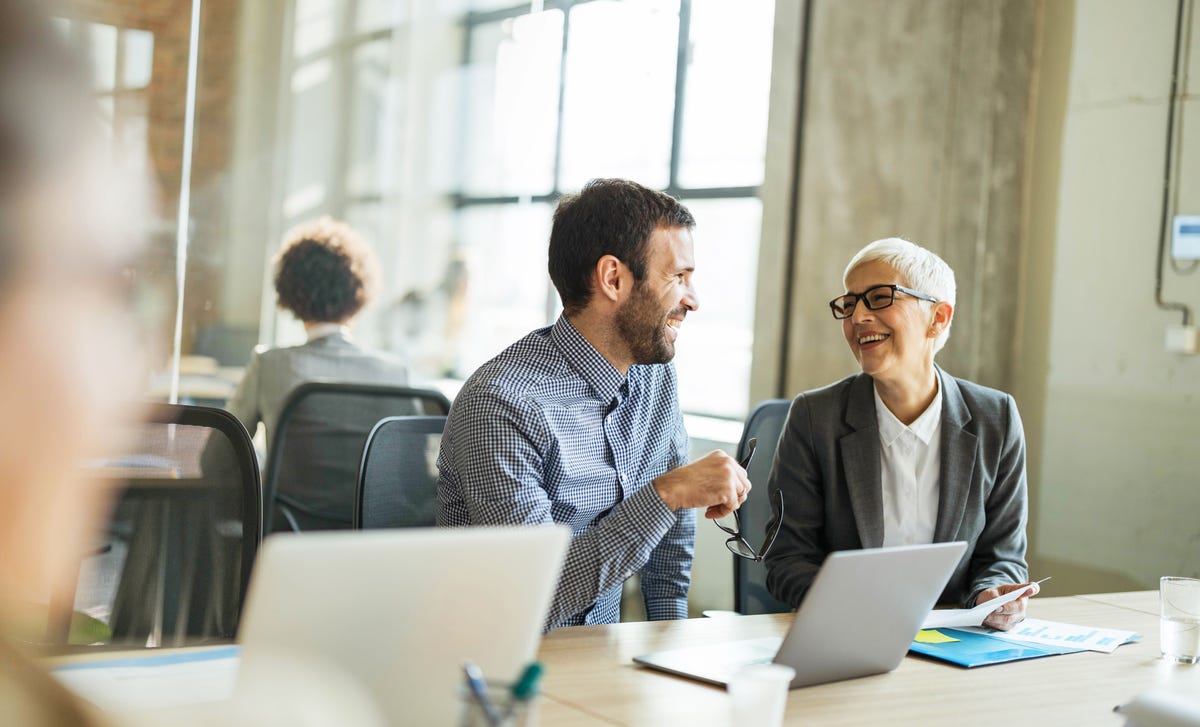 Dos colegas ríen y conversan amistosamente en un ambiente de oficina.