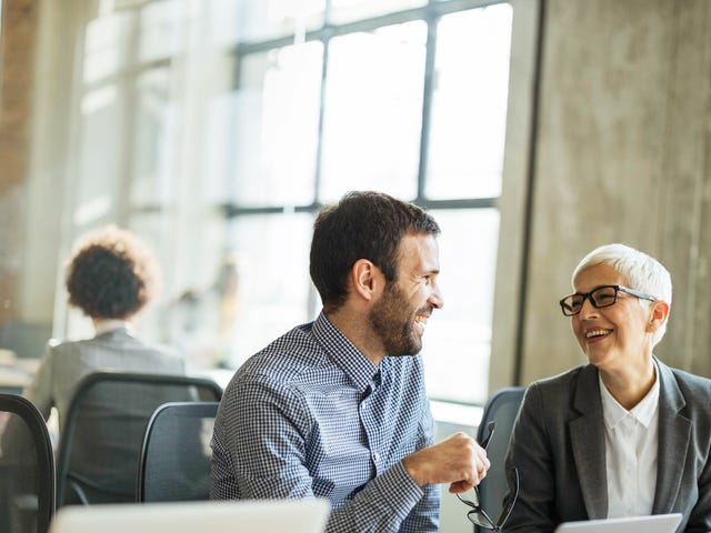 Dos colegas ríen y conversan amistosamente en un ambiente de oficina.