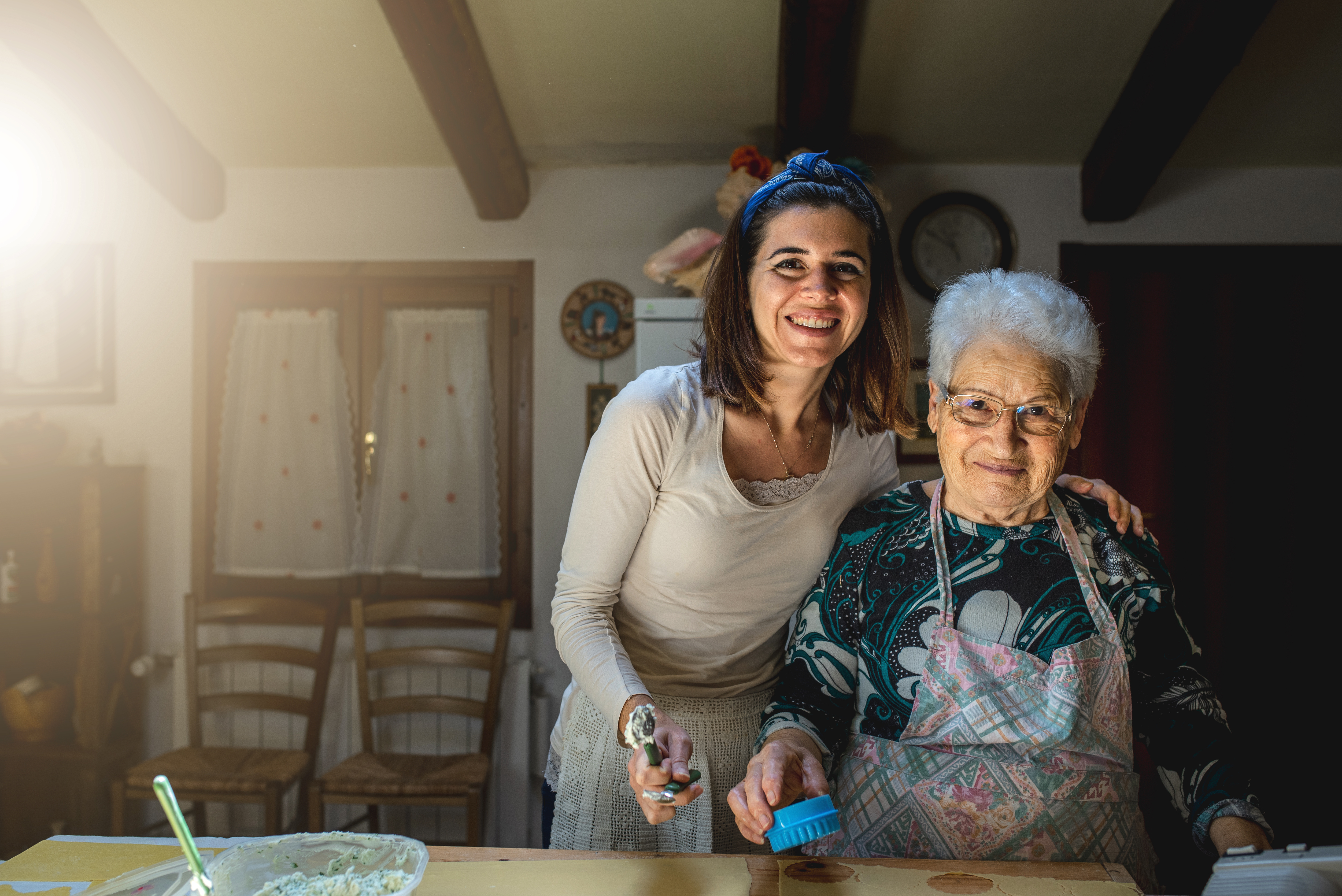 Joven nieta y su abuela sonriendo felices juntas en la cálida cocina de su hogar.