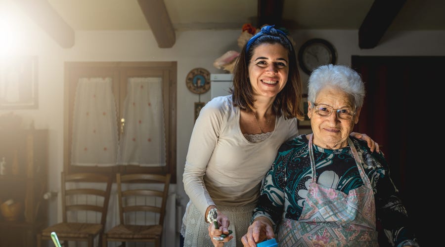 Joven nieta y su abuela sonriendo felices juntas en la cálida cocina de su hogar.