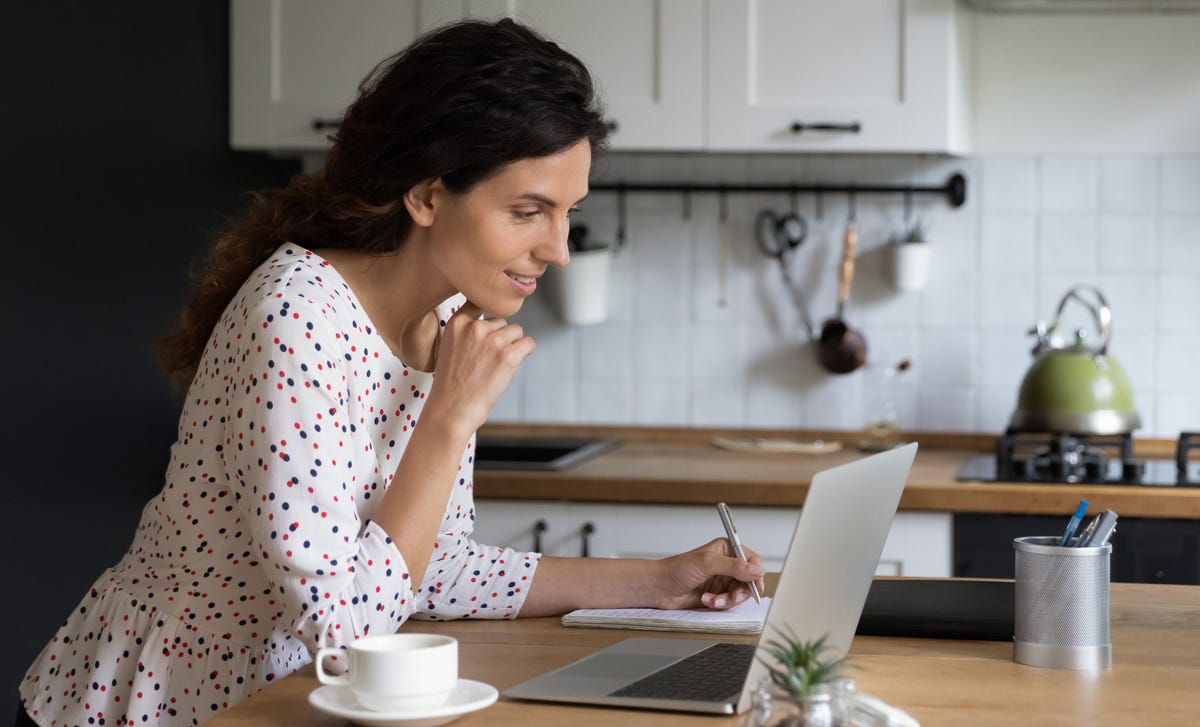 Mujer aprende idiomas online Berlitz, toma notas en su cocina.