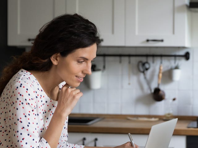 Mujer aprende idiomas online Berlitz, toma notas en su cocina.