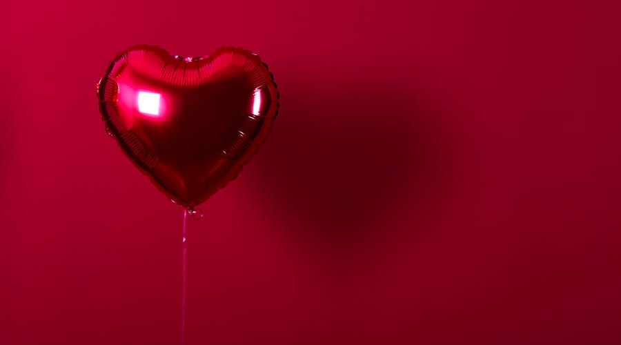 Globo brillante en forma de corazón rojo sobre fondo rojo, símbolo de amor.