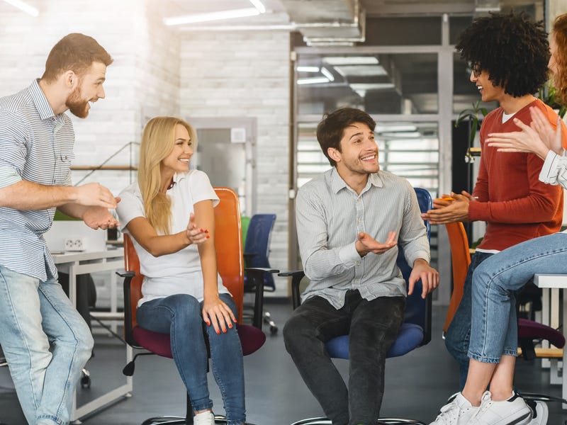 Grupo de colegas sonríe en oficina, comunicándose eficazmente, habilidades de idiomas Berlitz.