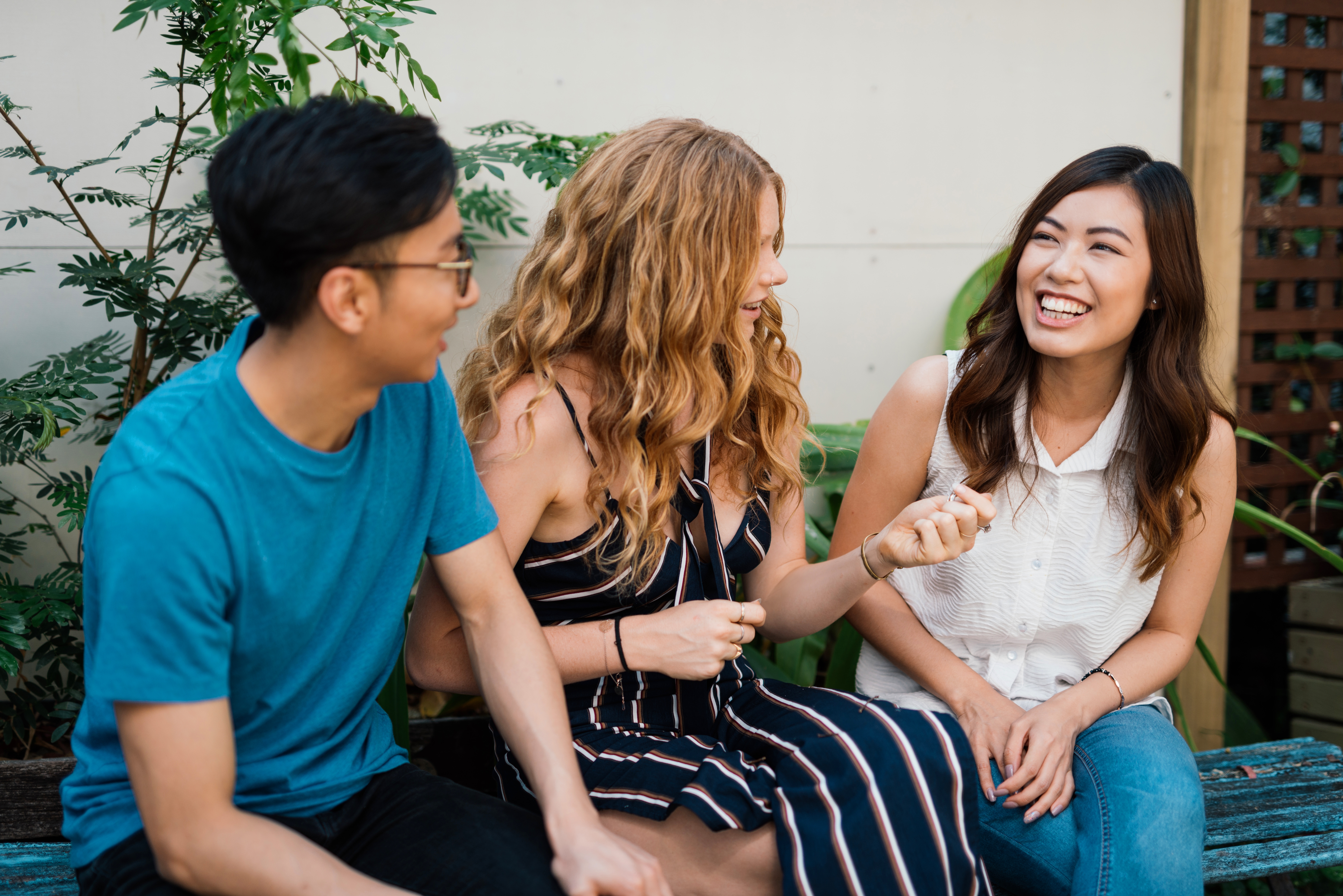 Tres jóvenes amigos de diversas etnias conversan y ríen al aire libre.