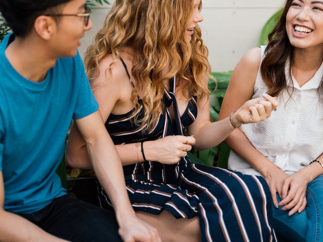 Tres jóvenes amigos de diversas etnias conversan y ríen al aire libre.
