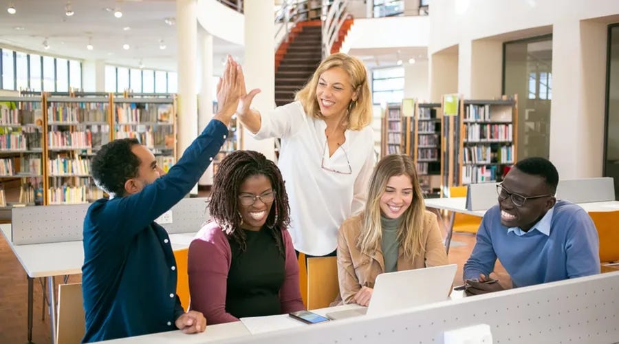 Grupo de estudiantes diversos y su profesora celebrando el éxito académico en la biblioteca.