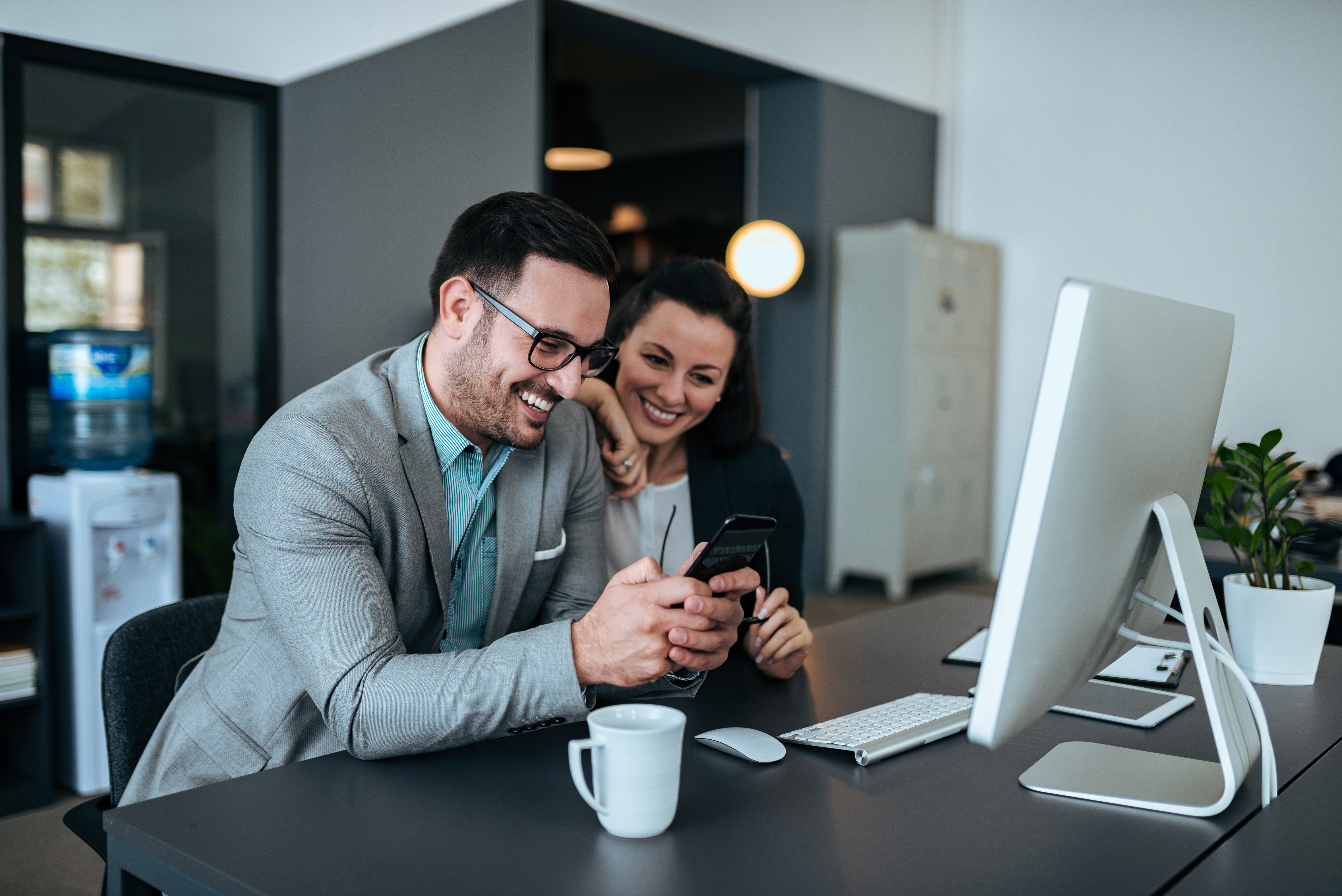 Dos colegas sonrientes mirando un teléfono en la oficina.