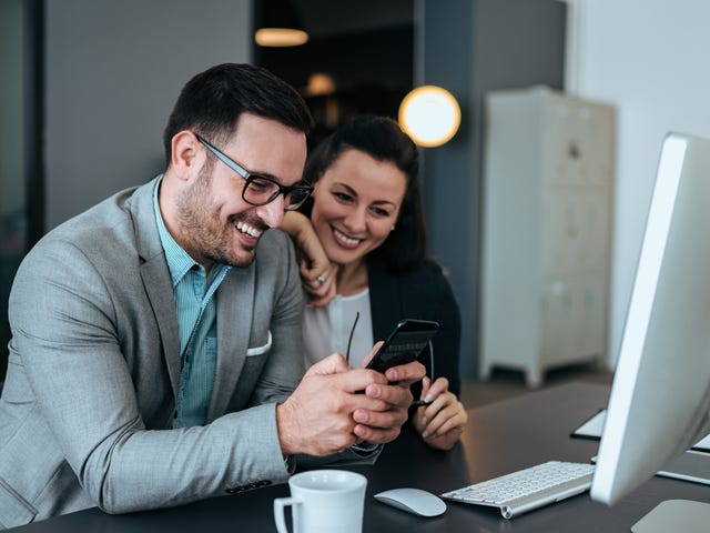 Dos colegas sonrientes mirando un teléfono en la oficina.